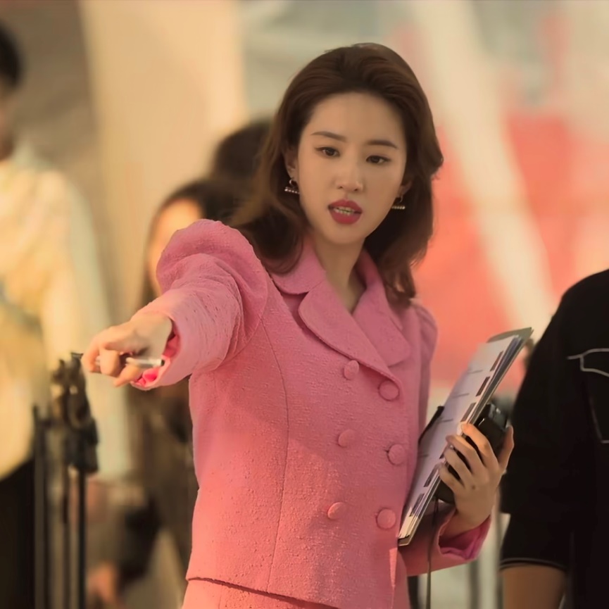 A person in a pink suit pointing her finger Description automatically generated
